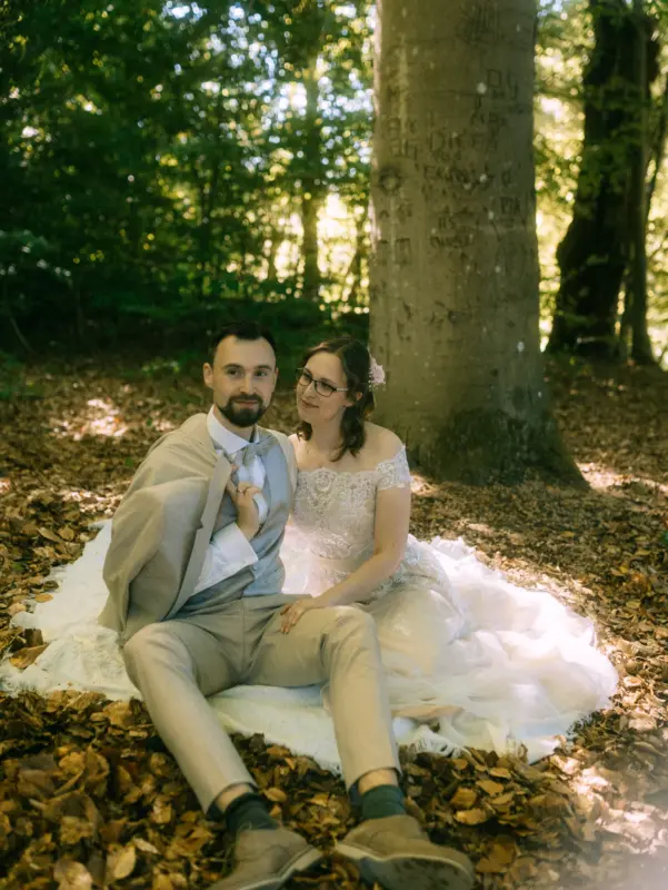 Ein Brautpaar sitzt auf einer Decke im herbstlichen Wald beim Schloss Basthorst, fotografiert von Hochzeitsfotograf Jan Büchler aus Crivitz. Der Bräutigam im hellen Anzug hält sein Sakko über der Schulter, während die Braut in einem Spitzenkleid liebevoll zu ihm aufschaut.