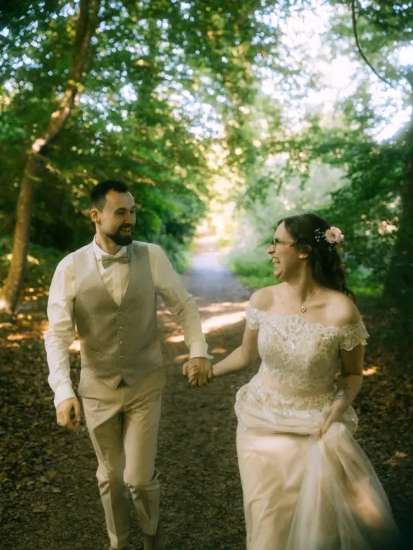Ein glückliches Brautpaar hält händchenhaltend inne und lacht sich während eines Spaziergangs im Wald am Schloss Basthorst bei Crivitz an. Dieses stimmungsvolle Hochzeitsfoto wurde von dem Hochzeitsfotograf Jan Büchler aus Crivitz aufgenommen.