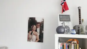 Ein an der Wand hängendes Hochzeitsfoto vom Schloss Basthorst, aufgenommen vom Hochzeitsfotograf Jan Büchler aus Crivitz. Das Bild zeigt ein glückliches Brautpaar in einer romantischen Umarmung im Freien, platziert neben einem Regal mit Dekoartikeln und einem gerahmten Spruch.